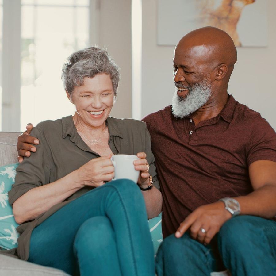 Settle into comfort at William Booth Towers smiling, older couple, sit together on a couch